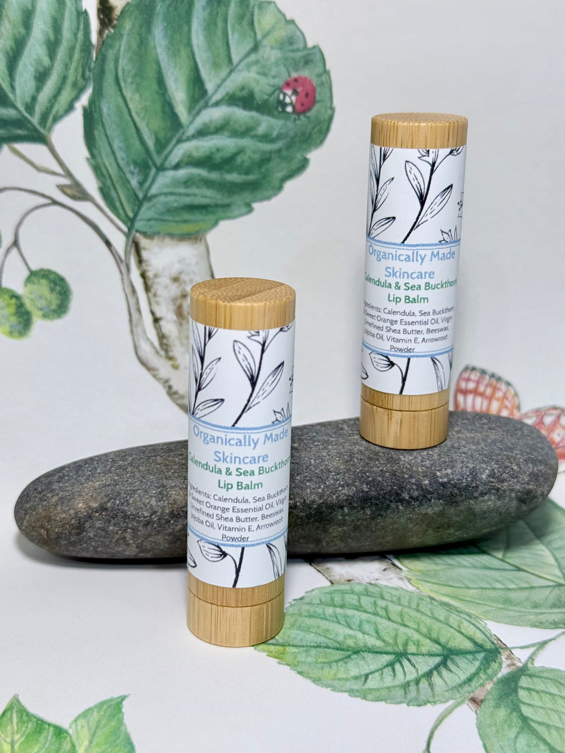 Two Organically Made Skincare Calendula & Sea Buckthorn Lip Balm tubes displayed on stones with botanical styling